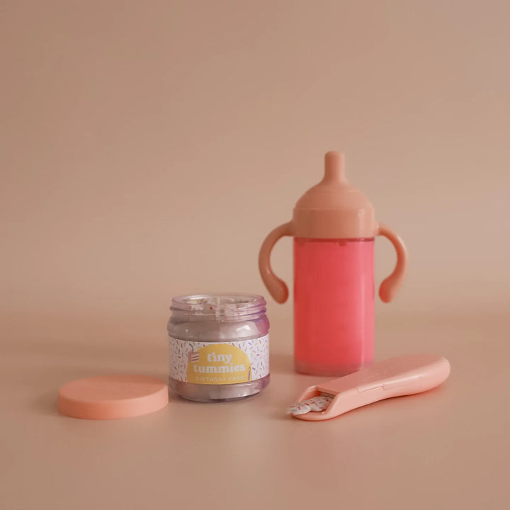 Pink sippy cup, jar, and spoon on a beige background