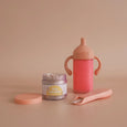 Pink sippy cup, jar, and spoon on a beige background