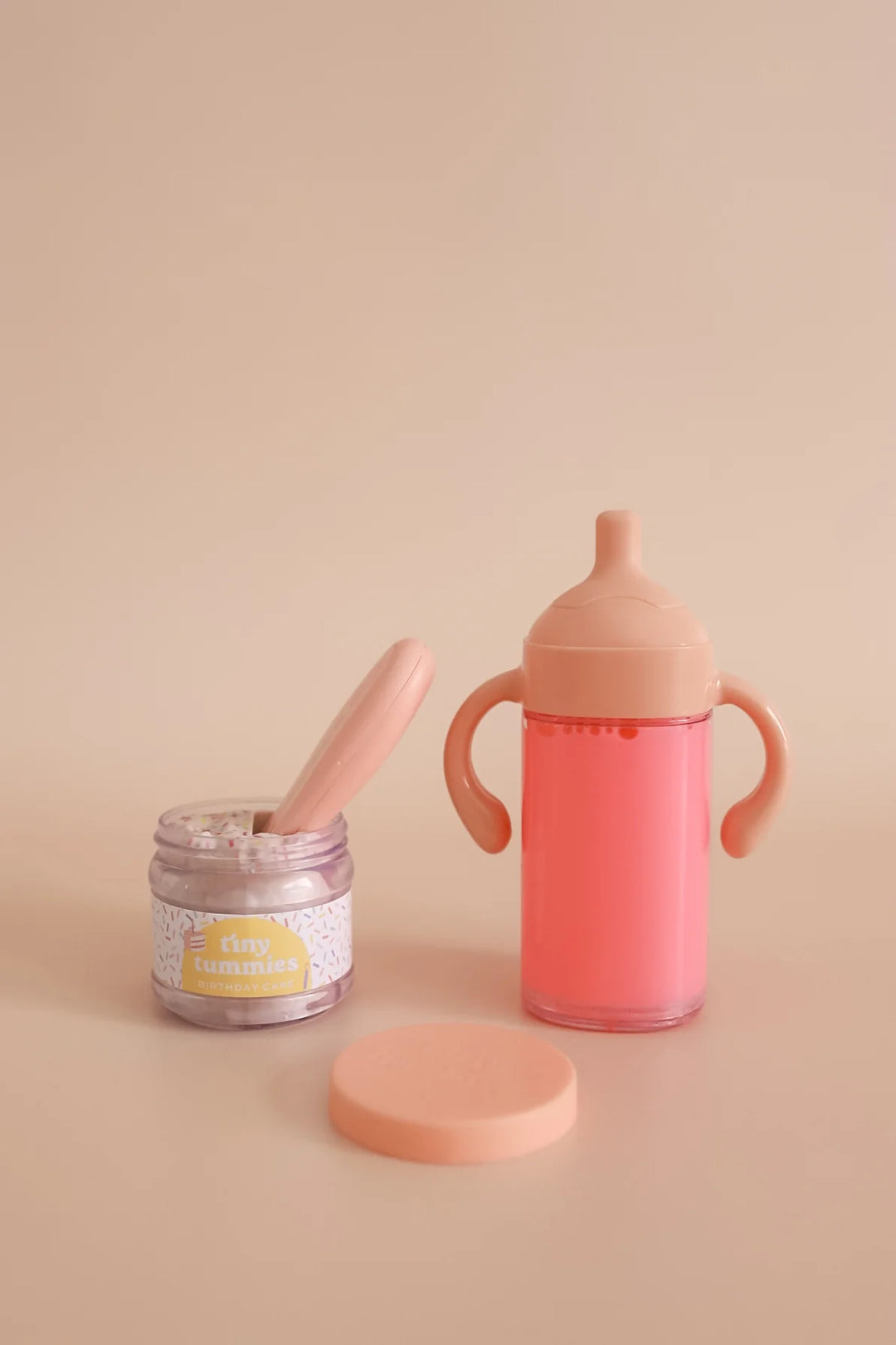 Pink baby bottle, jar, and spoon on a beige background