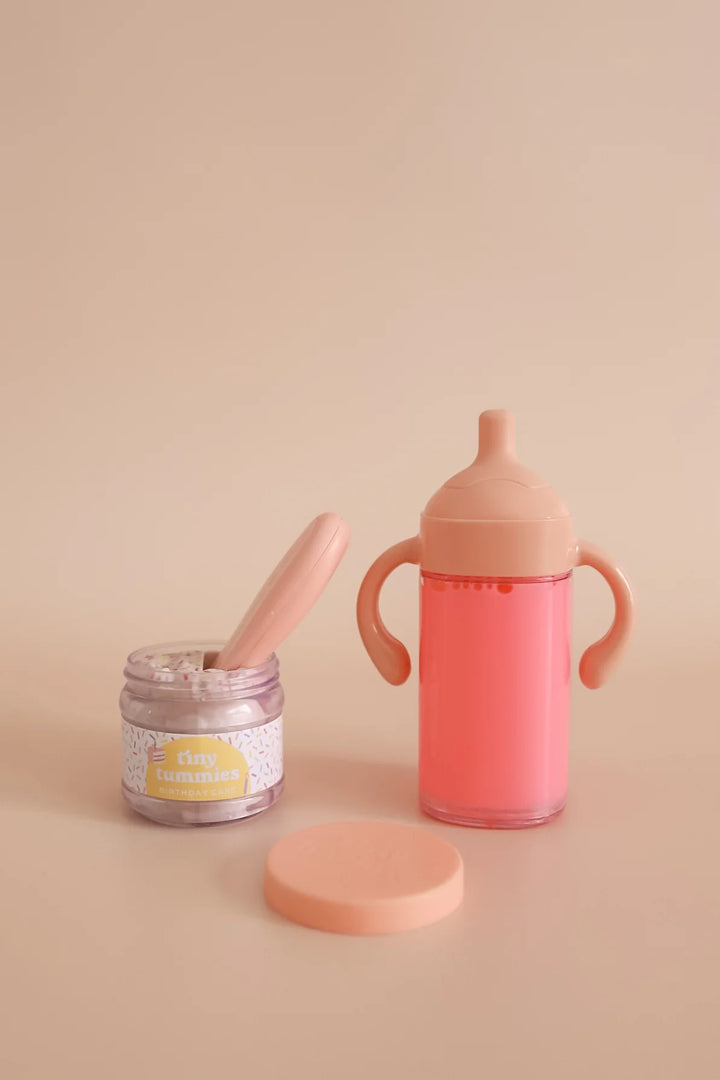 Pink baby bottle, jar, and spoon on a beige background