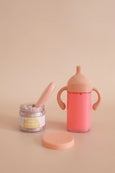 Pink baby bottle, jar, and spoon on a beige background