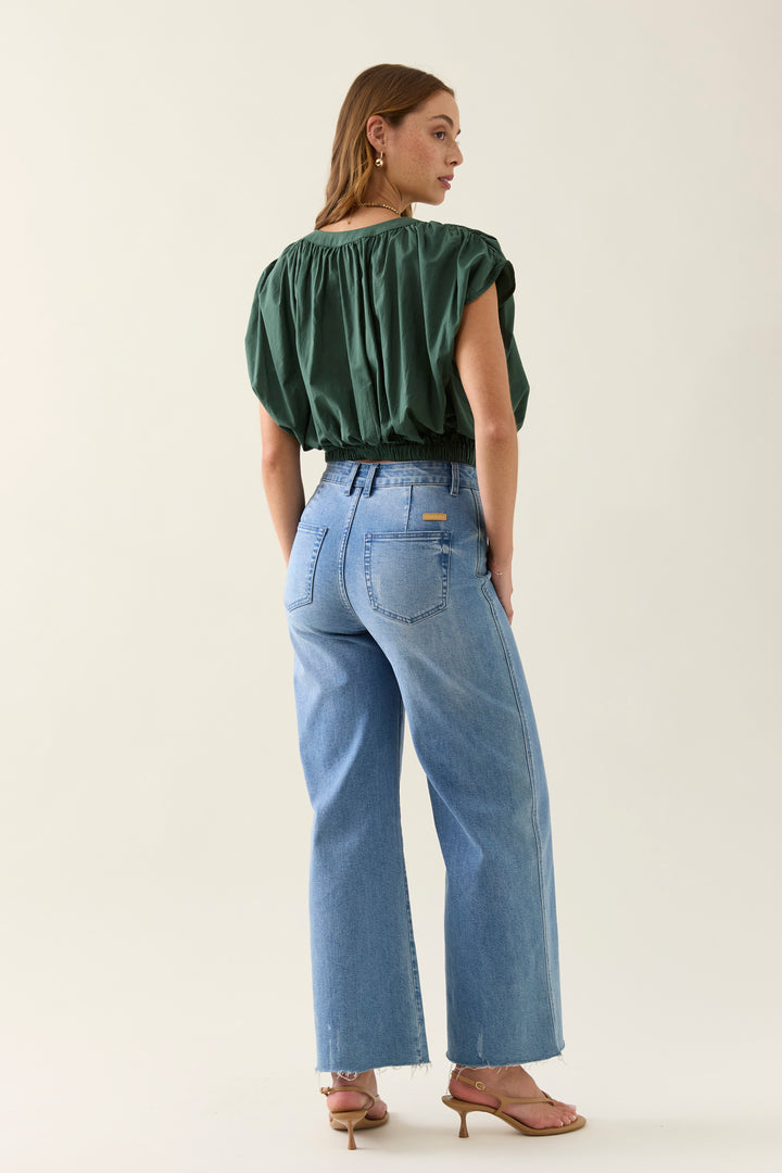 Woman wearing a green isle of mine top and blue jeans on a plain background