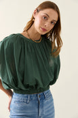 Woman wearing a green isle o mine blouse and blue jeans against a plain background