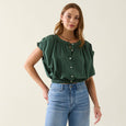 Woman wearing a green isle of mine top and blue jeans on a plain background