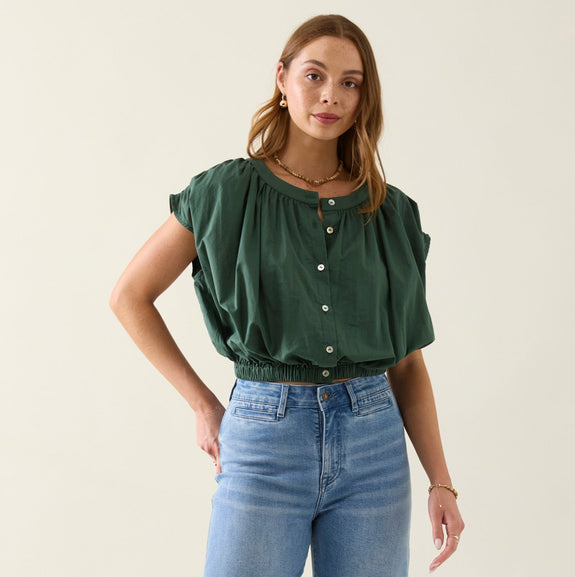 Woman wearing a green isle of mine top and blue jeans on a plain background