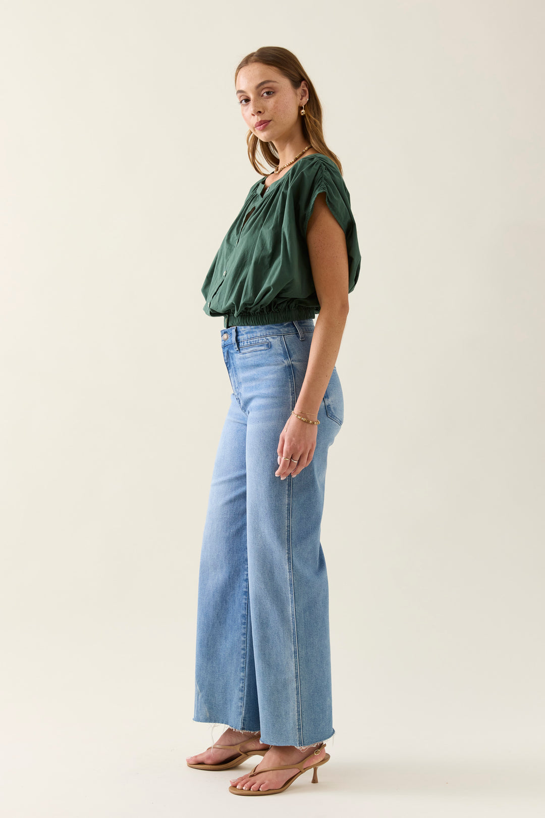 Woman wearing a green isle of mine top and blue jeans on a white background
