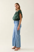 Woman wearing a green isle of mine top and blue jeans on a white background